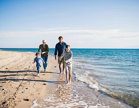 A family of four walks along a sunny beach, waves lapping at their feet, as they enjoy a seaside stroll together.